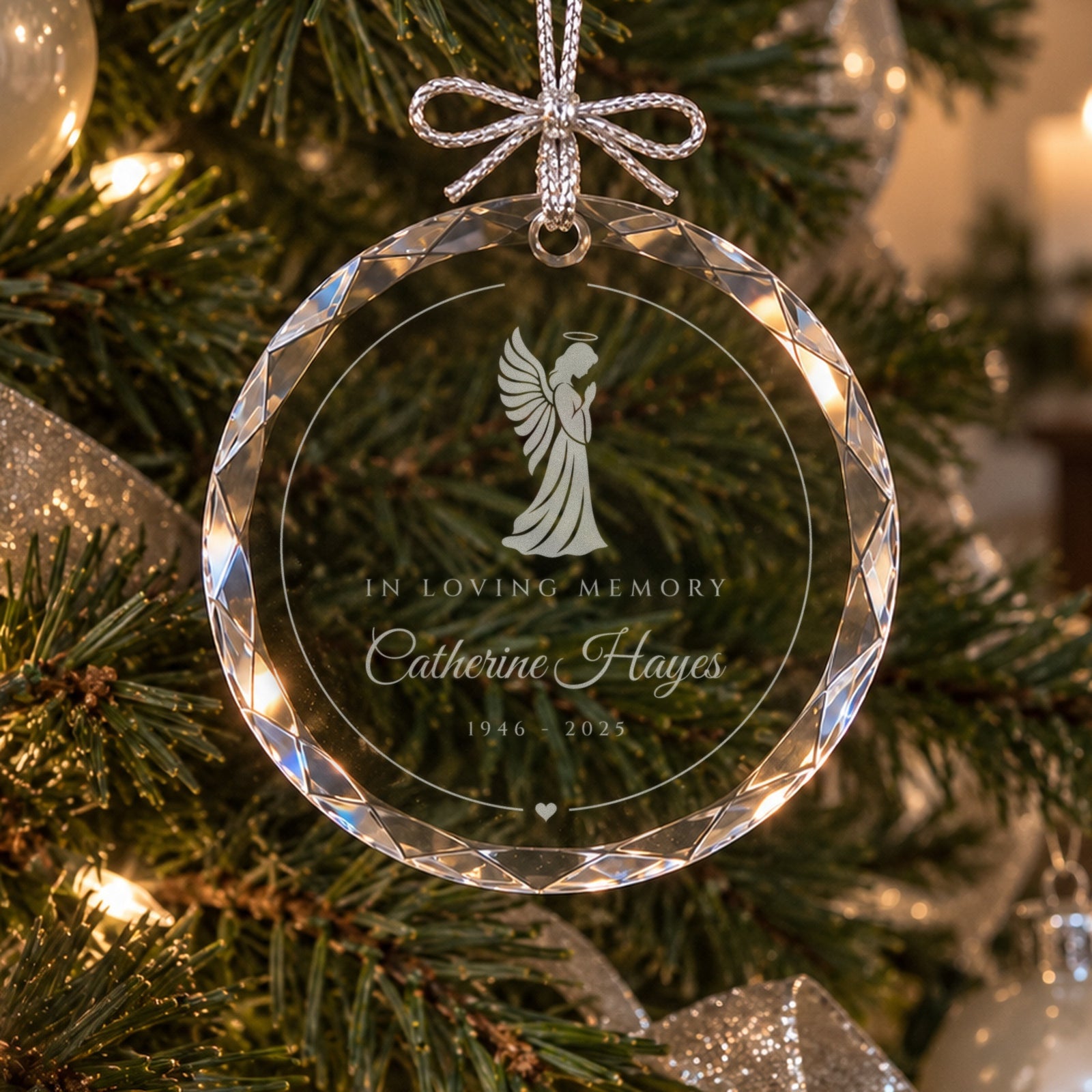 Personalized angel memorial ornament in faceted glass on a lit green Christmas tree with silver ribbon, engraved In Loving Memory, Catherine Hayes, 1946 to 2025