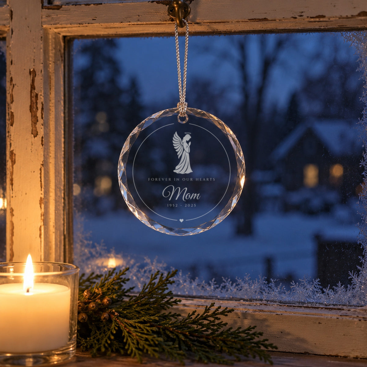 Angel memorial Christmas ornament hanging in a snowy window beside a lit candle, engraved with a praying angel, Forever in Our Hearts and Mom