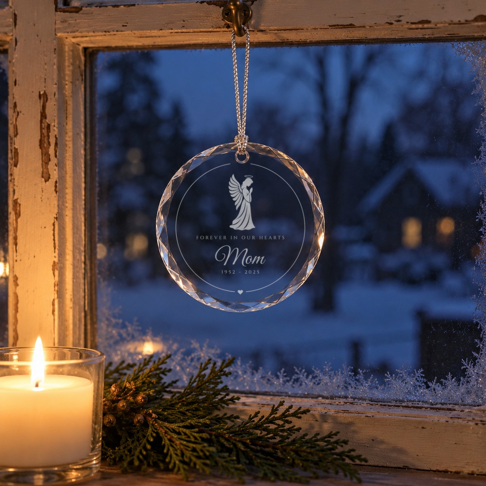 Angel memorial Christmas ornament hanging in a snowy window beside a lit candle, engraved with a praying angel, Forever in Our Hearts and Mom