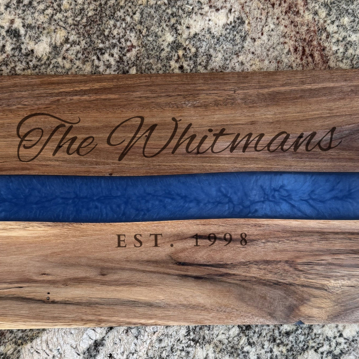 Close-up of the laser engraving on the acacia serving tray: The Whitmans in script above the blue pearl resin river and EST. 1998 in capitals below