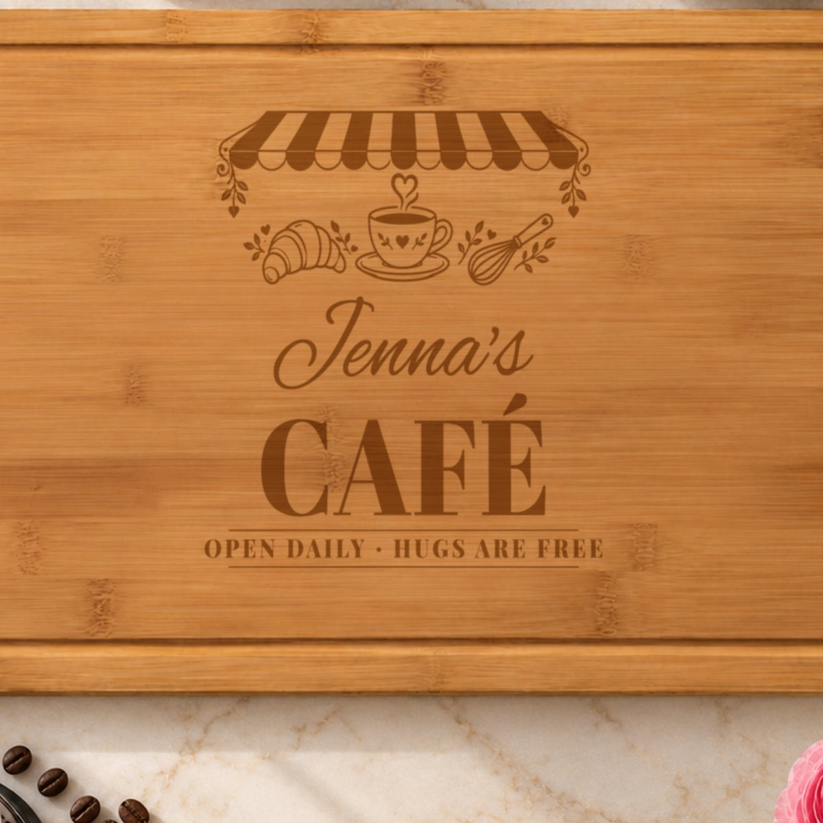 Close-up of the laser engraving on the cafe cutting board: the striped awning, heart-steam coffee cup, Jenna's in script and CAFÉ