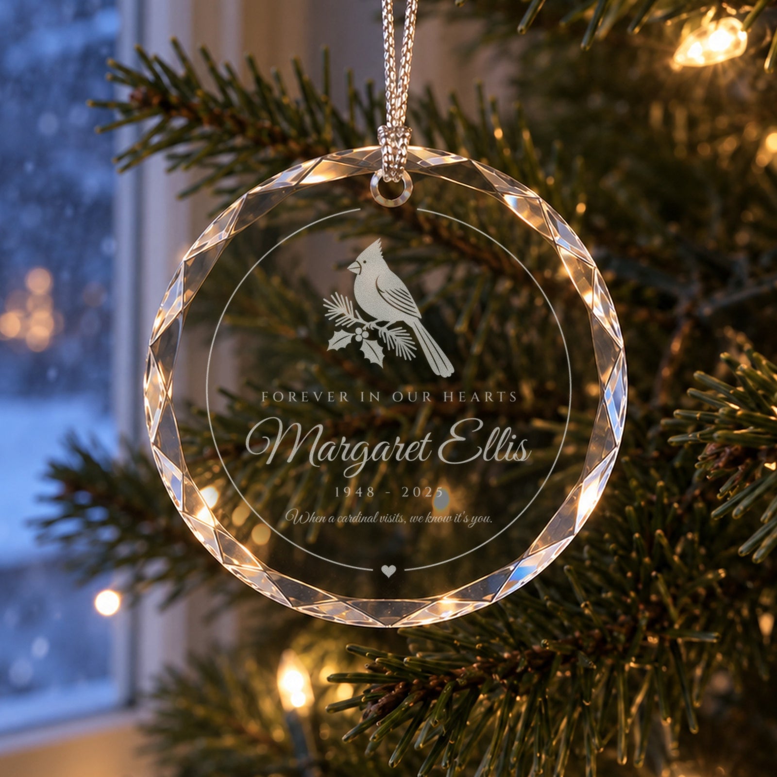 Personalized cardinal memorial ornament in faceted glass on a Christmas tree by a snowy window, engraved Forever in Our Hearts, Margaret Ellis, 1948 - 2025