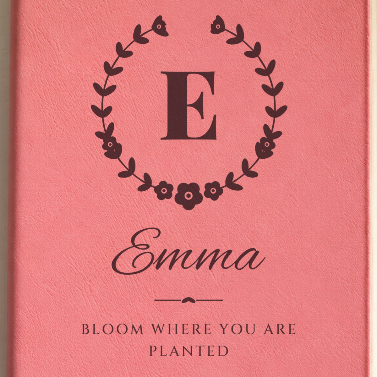 Close-up of the engraving on the wildflower crest journal: the initial E in a floral wreath, Emma in script and Bloom Where You Are Planted