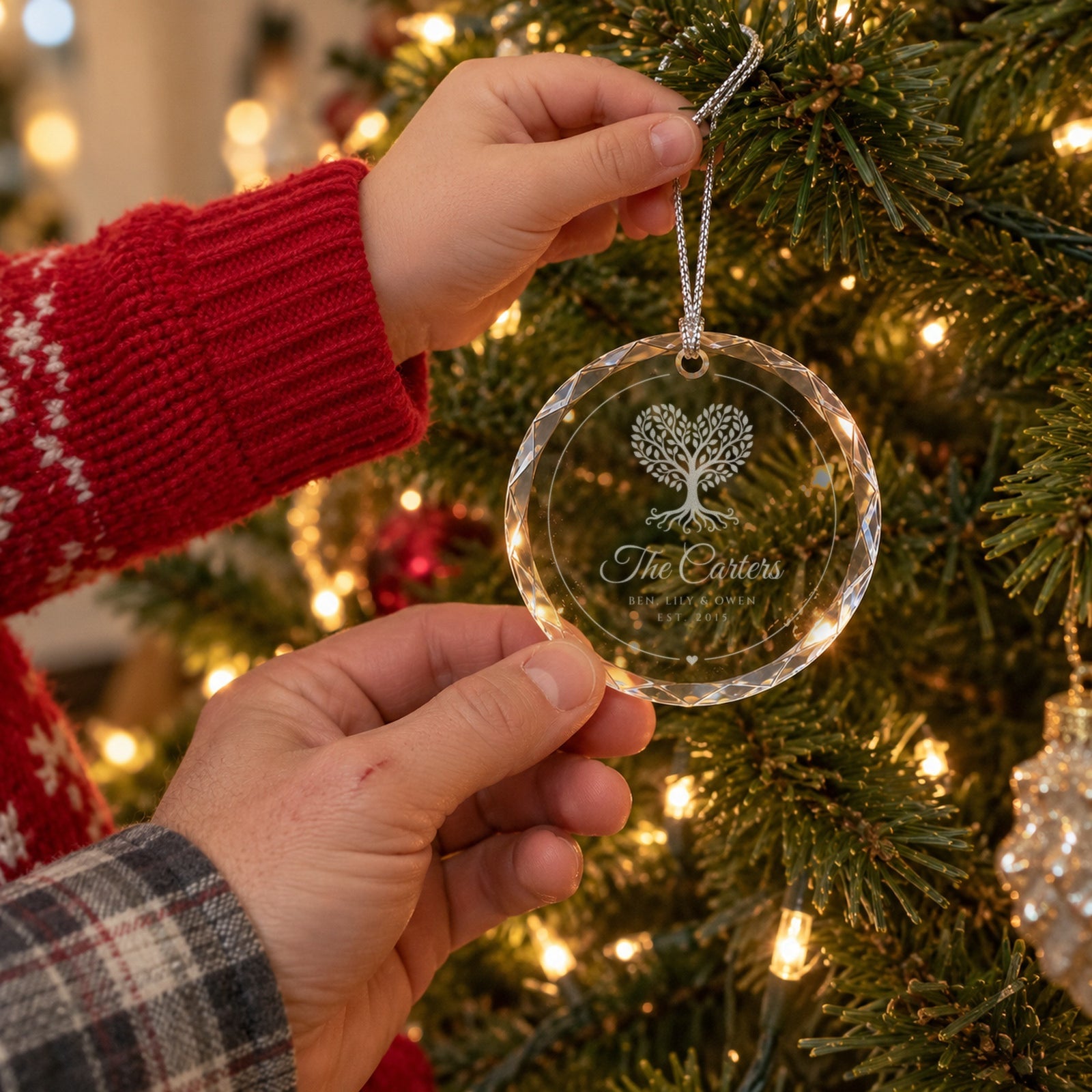 A parent and child hanging the engraved family tree Christmas ornament together, reading The Carters, Ben, Lily and Owen, EST. 2015