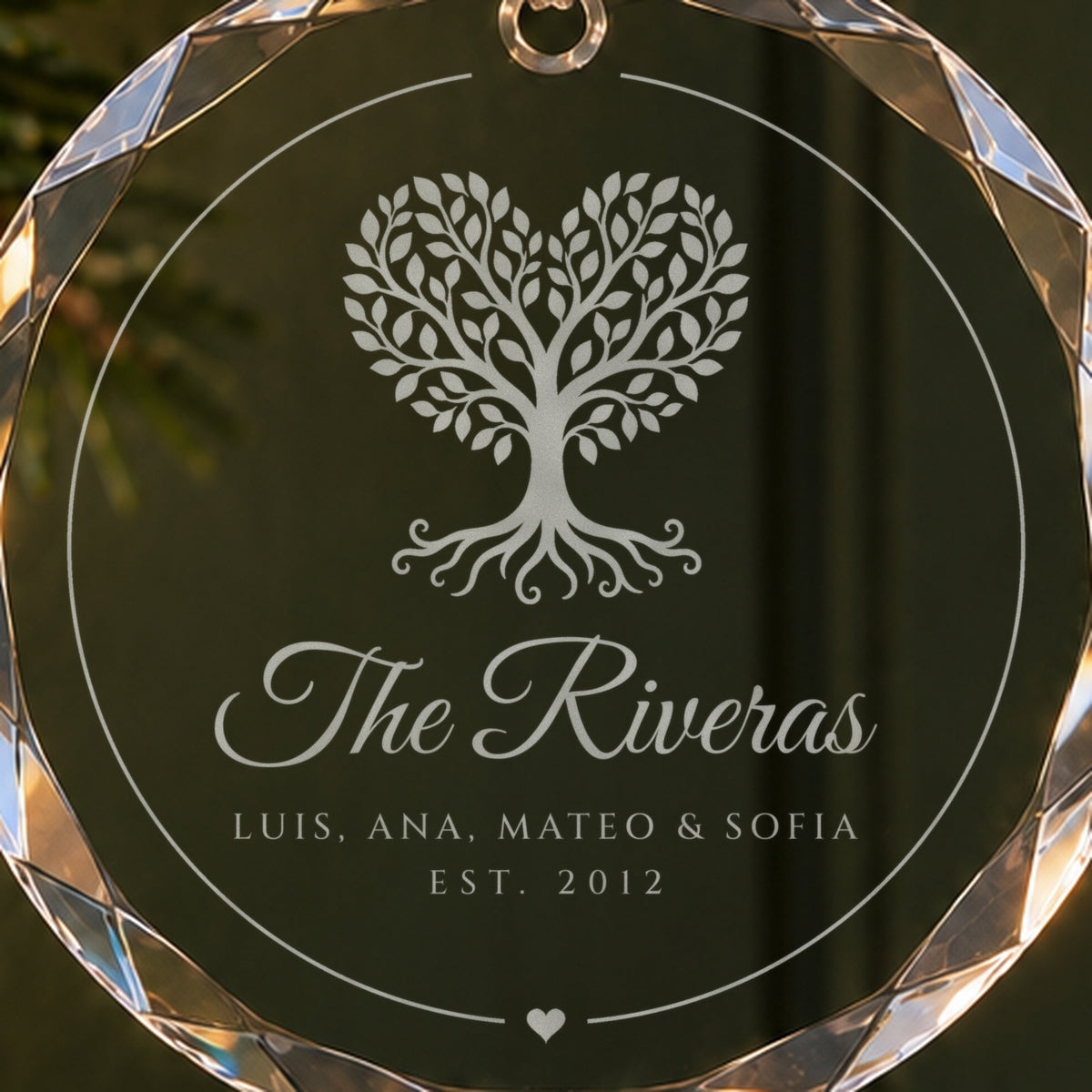 Close-up of the frosted heart-shaped family tree engraving on the glass ornament, with The Riveras, four first names and EST. 2012