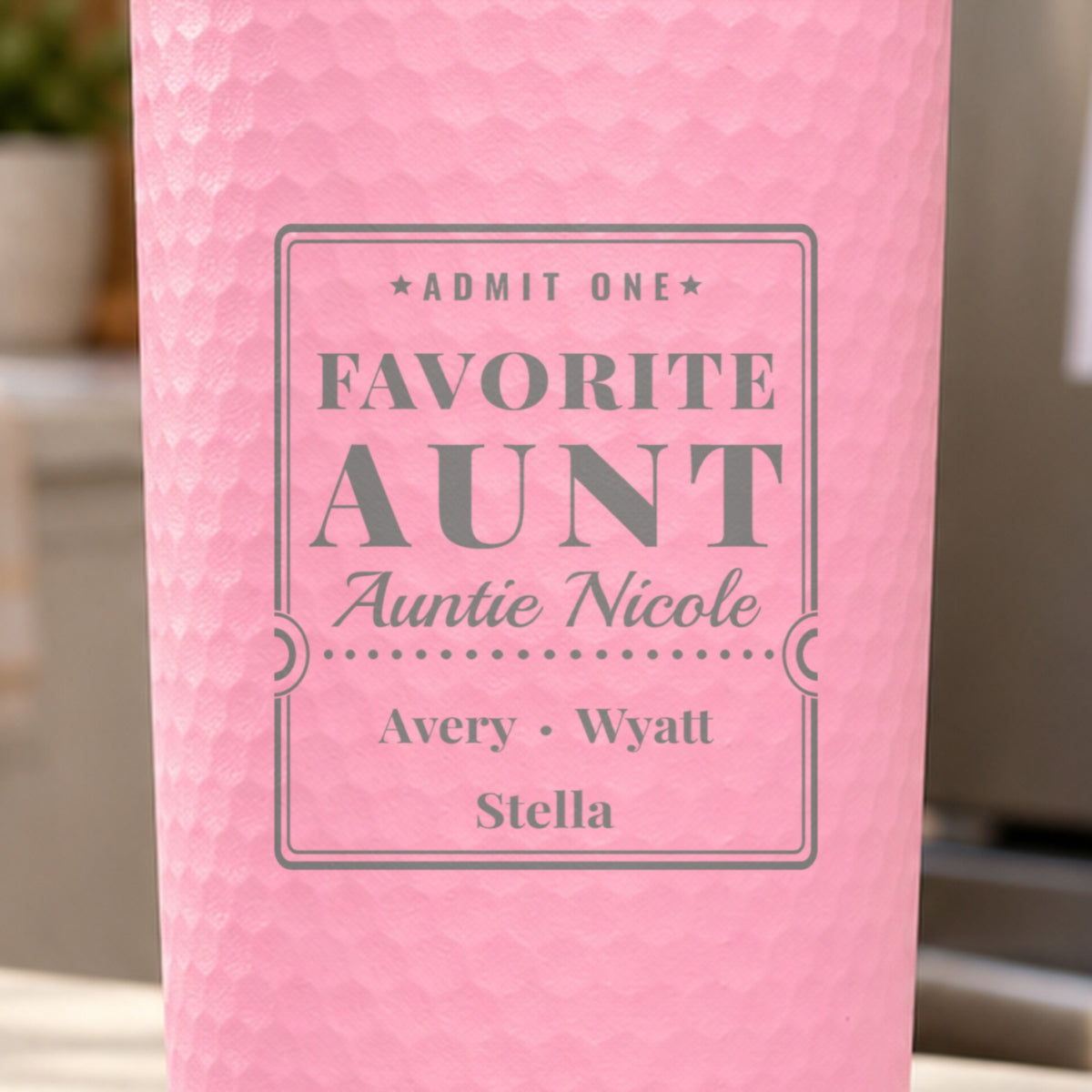 Close-up of the laser engraving on a pink dimpled tumbler: Admit One, Favorite Aunt, Auntie Nicole, Avery, Wyatt and Stella