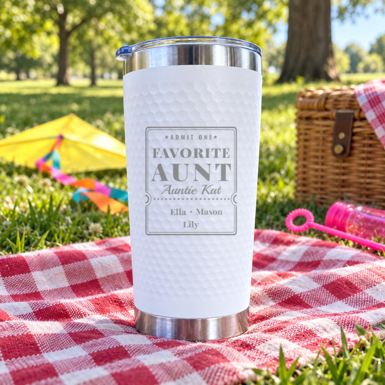 White dimpled tumbler engraved Favorite Aunt for Auntie Kat with nieces and nephews Ella, Mason and Lily, on a park picnic blanket