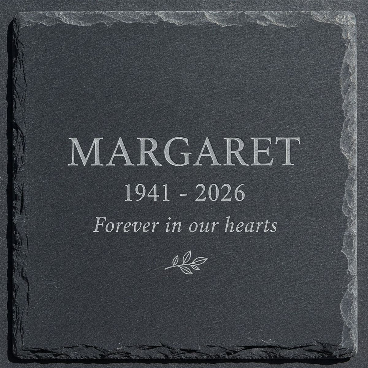 Close view of the recessed laser engraving on a natural slate memorial garden stone, the sample name Margaret cut pale into the dark stone above the years