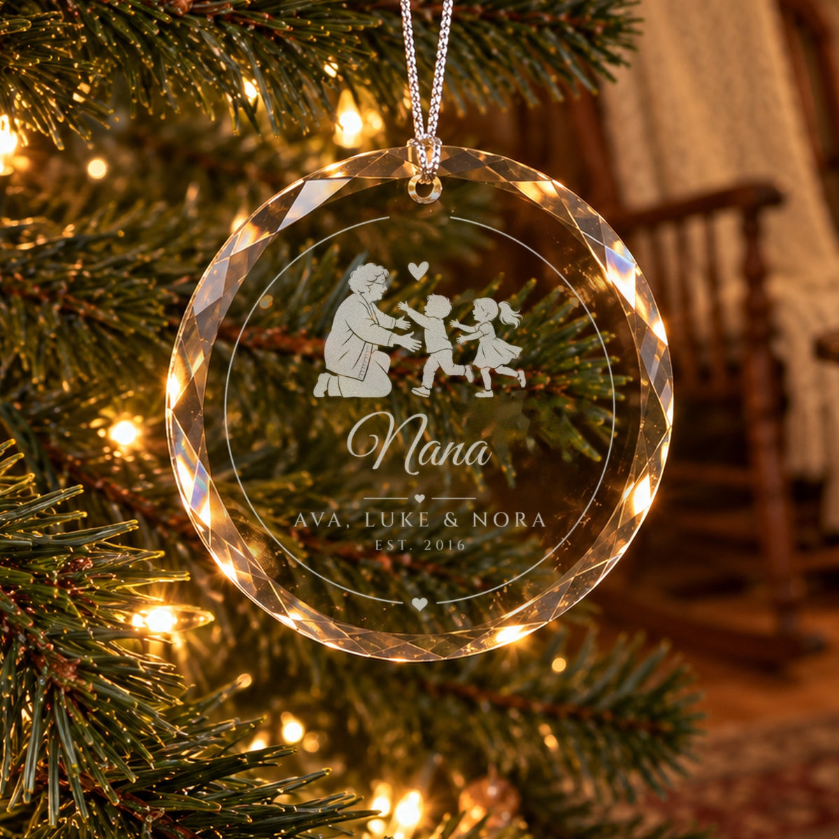Personalized grandma Christmas ornament in faceted glass on a lit tree, engraved with a grandmother hugging two grandkids, Nana in script and AVA, LUKE &amp; NORA, EST. 2016