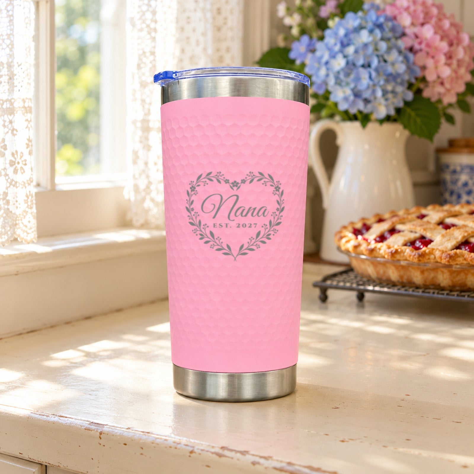 Pink textured tumbler engraved with a heart wreath around the name Nana and EST. 2027, a personalized gift for grandma in a sunny kitchen