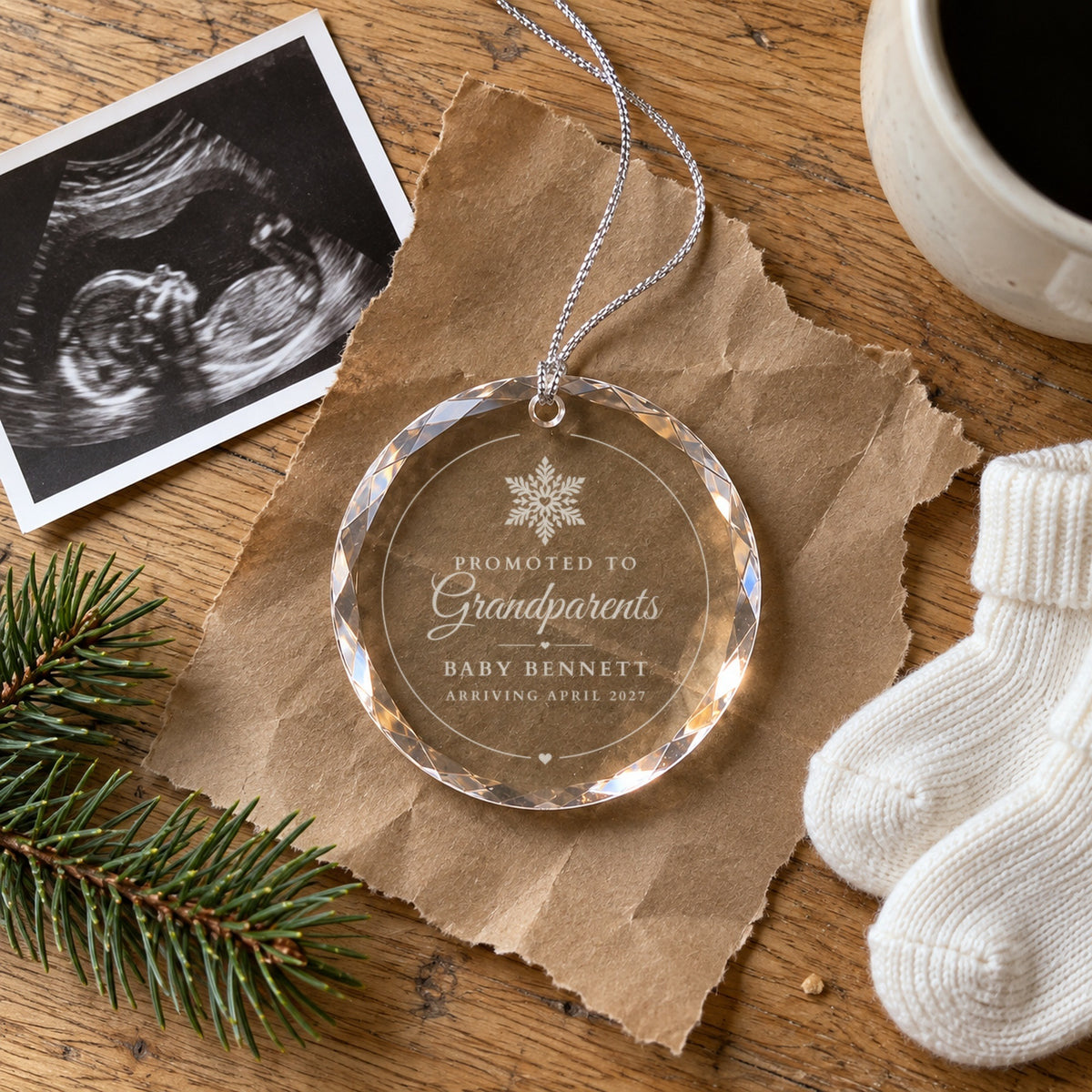 Promoted to Grandparents ornament on brown kraft paper beside an ultrasound photo and tiny white baby socks, engraved Baby Bennett, Arriving April 2027