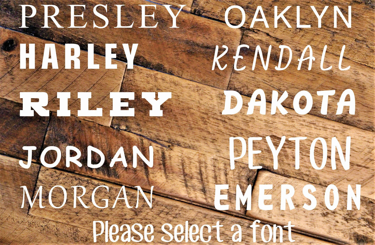 Font chart for the engraved baby girl spoon set showing all 10 hand-lettered font options including Presley, Oaklyn, Harley, Kendall, Riley, Dakota, Jordan, Peyton, Morgan and Emerson on a wood background.
