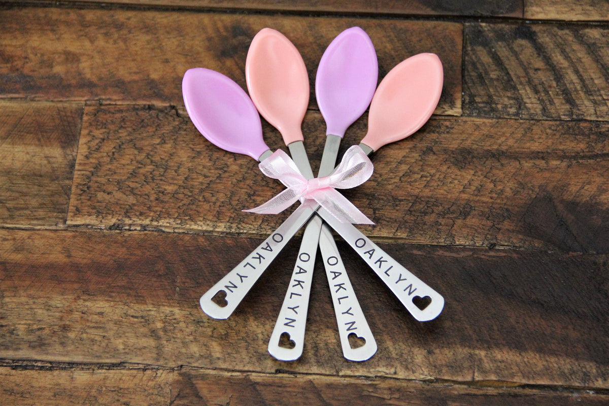 Personalized baby girl spoon set in pink and purple silicone tips, laser-engraved with the sample name Oaklyn and a small heart cutout at the end of each handle.