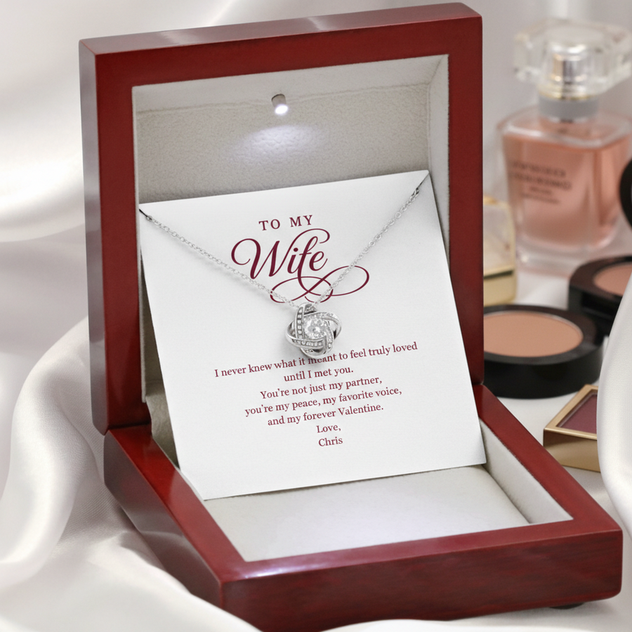 Red jewelry box with white card reading "TO MY Wife" and personalized message signed "Love, Chris," featuring silver knot pendant necklace on chain