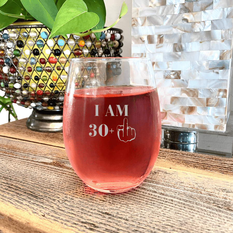 30s birthday stemless wine glass engraved 'I am 30+' with a middle finger graphic, filled with rosé wine indoors