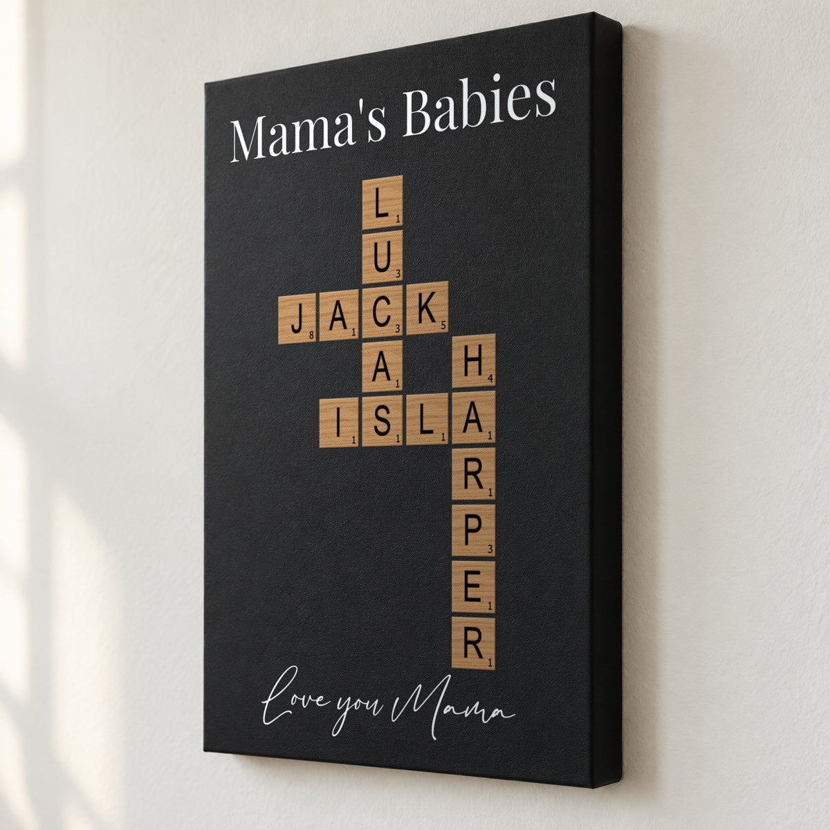 Angled close view of a Mama's Babies crossword sign showing the 1.5 inch deep edge and her kids' names printed flat on black leatherette