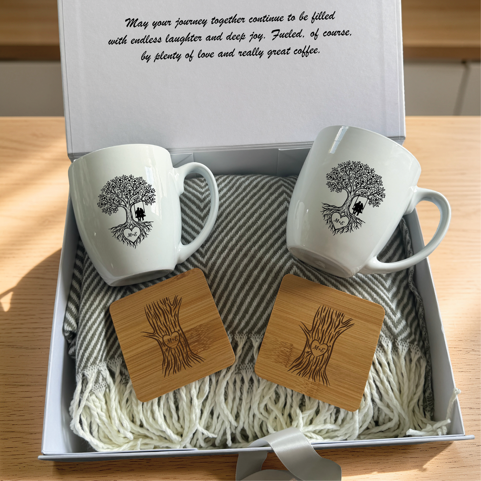 Couples gift box open to show a personalized message printed inside the lid above the engraved mugs, bamboo coasters and grey herringbone blanket.