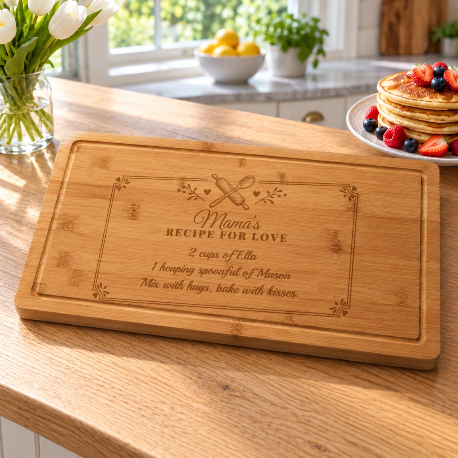 Personalized gift for mom: bamboo board engraved Mama's Recipe for Love with two kids' names, on a sunny kitchen island beside pancakes and tulips