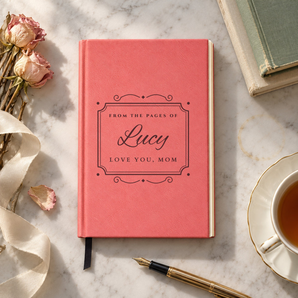 Personalized name journal for her in pink on a marble table, engraved FROM THE PAGES OF Lucy in script with Love You, Mom inside a bookplate frame