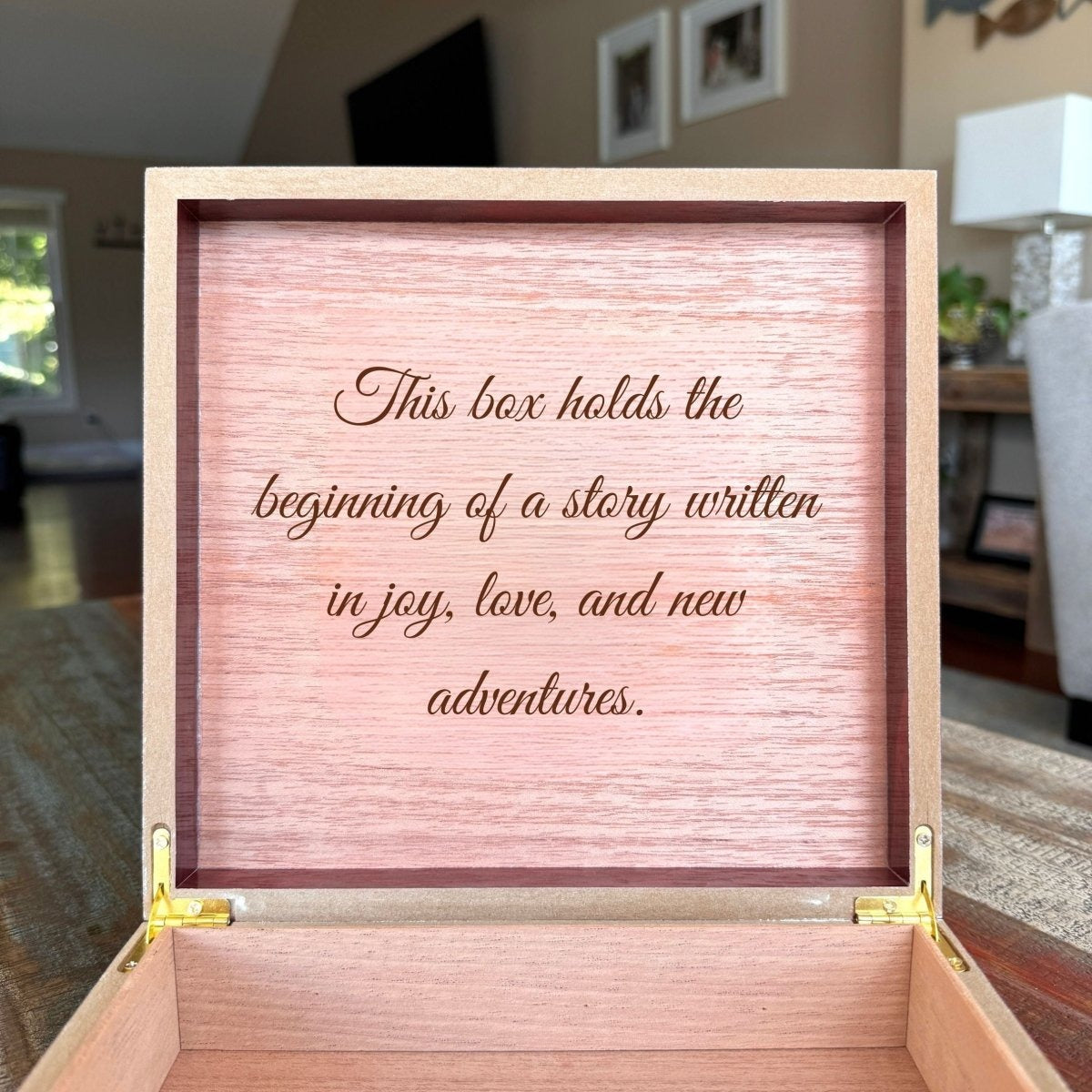 Close view inside an open newborn keepsake box, the lid engraved in script with a sample message about a story written in joy, love and new adventures