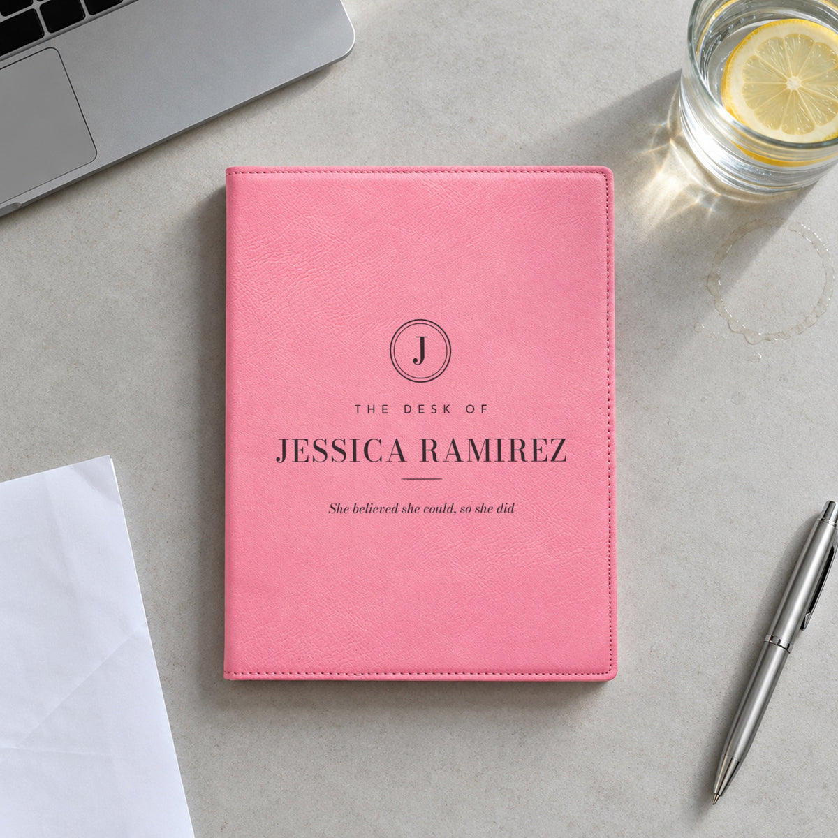 Pink engraved padfolio reading The Desk of Jessica Ramirez with the quote She believed she could, so she did, on an office meeting table