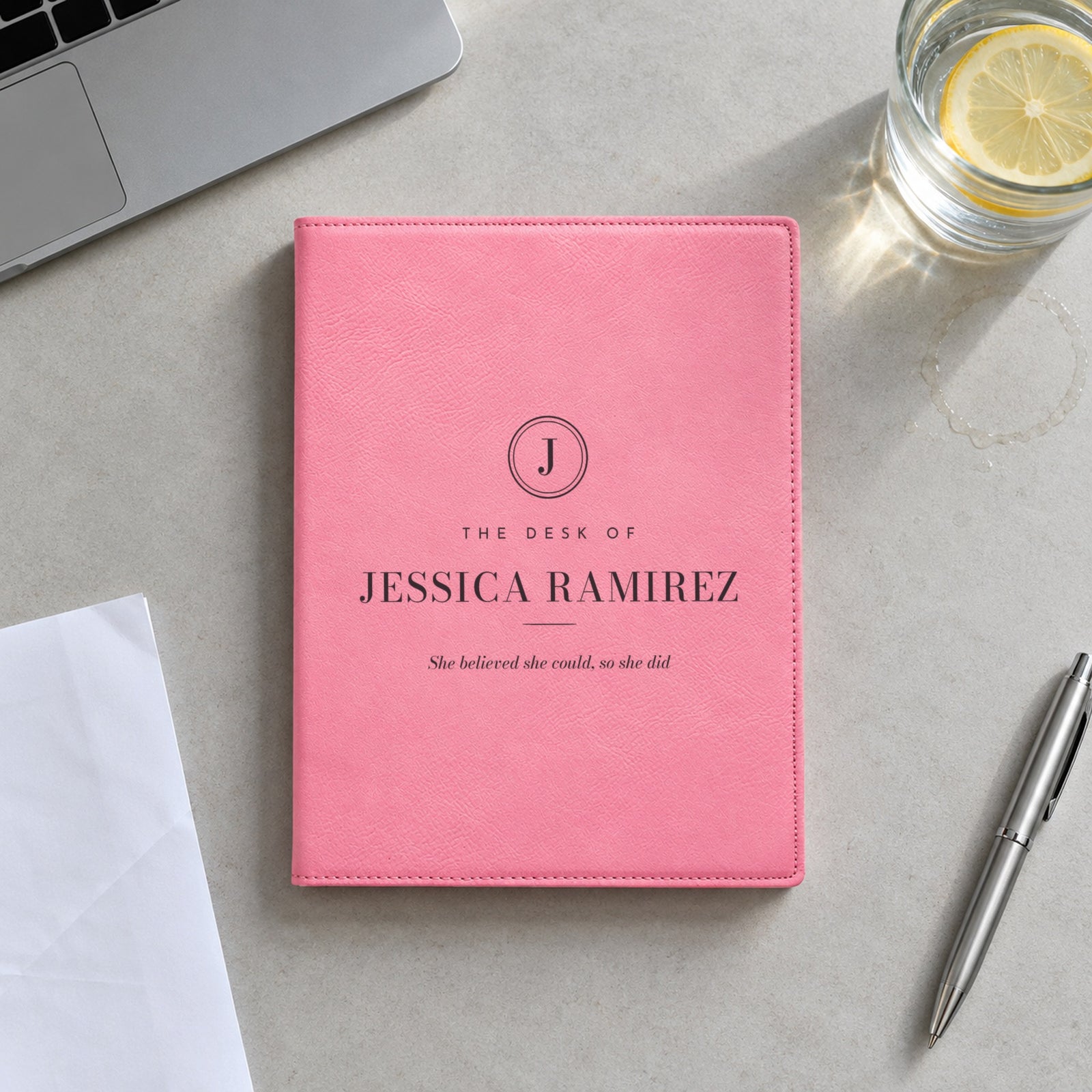 Pink engraved padfolio reading The Desk of Jessica Ramirez with the quote She believed she could, so she did, on an office meeting table
