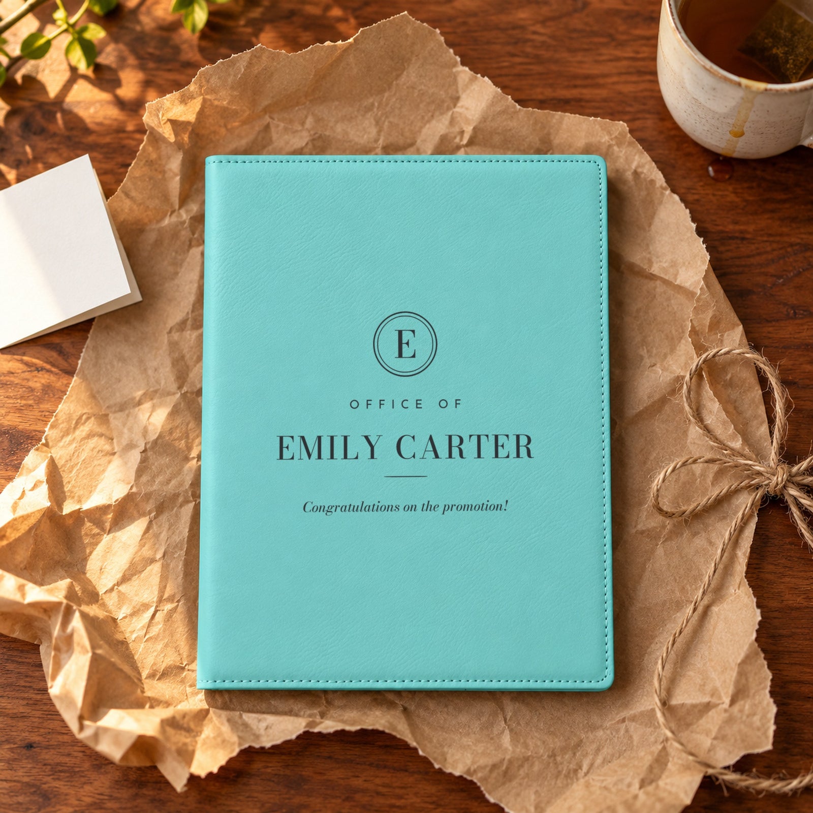 Teal monogram padfolio engraved Office of Emily Carter, Congratulations on the promotion, unwrapped on brown kraft paper as a promotion gift