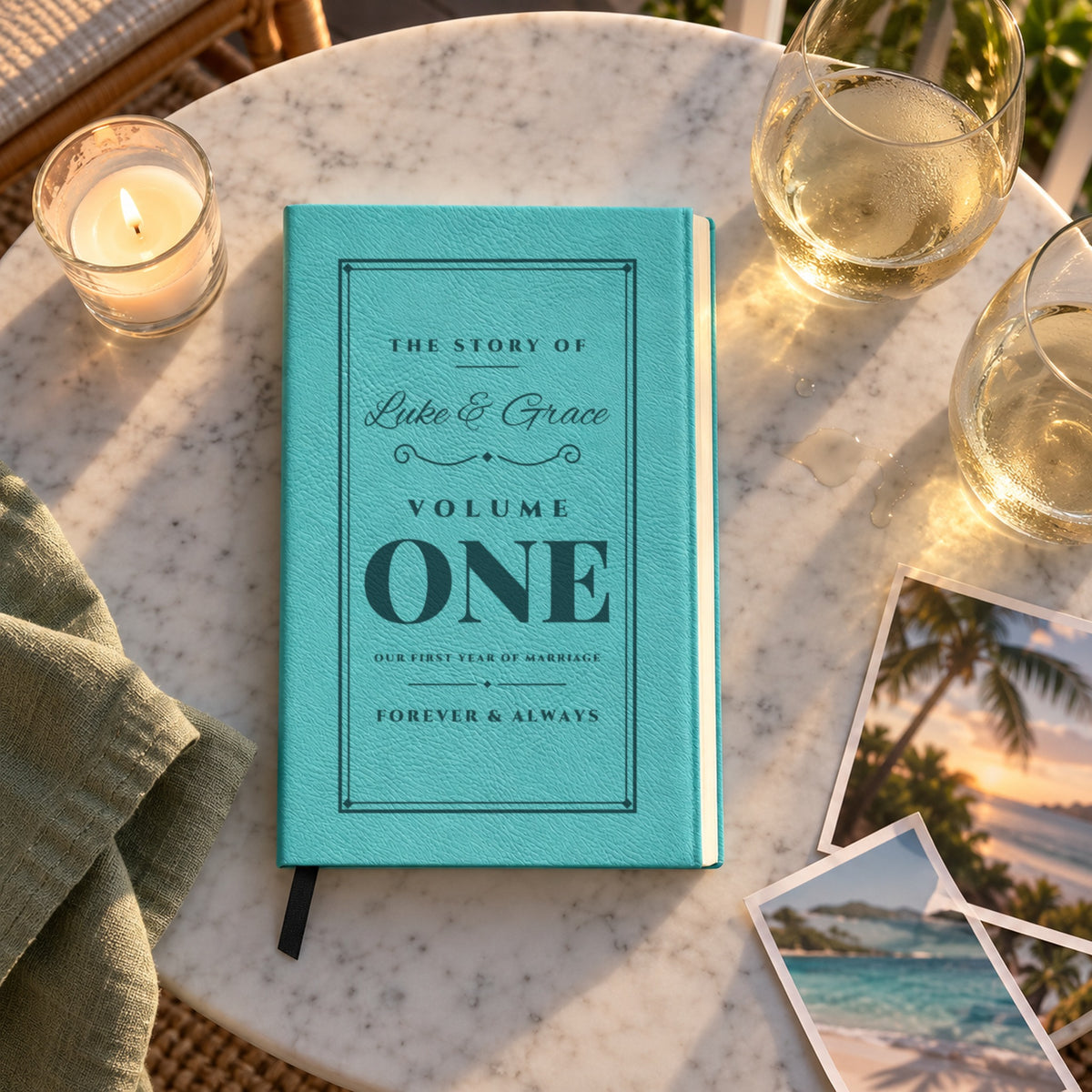 Teal paper anniversary gift journal engraved The Story Of Luke & Grace, Volume One, Forever & Always, on a porch table with two wine glasses