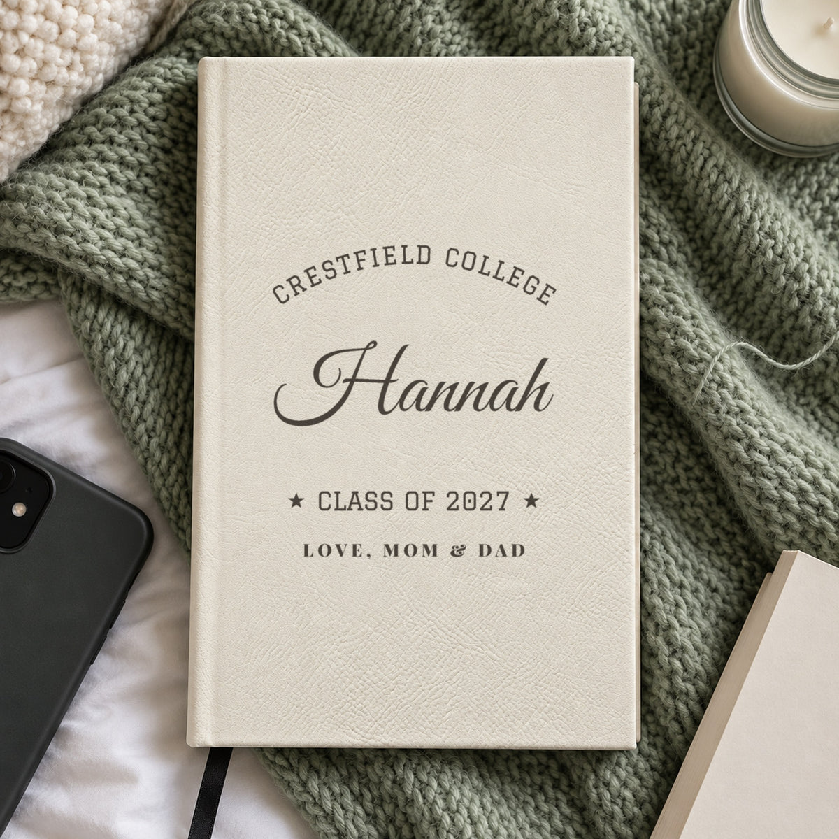 White journal engraved with Crestfield College arched over Hannah, Class of 2027 and Love, Mom &amp; Dad, on a sage knit blanket, a gift for a daughter in college