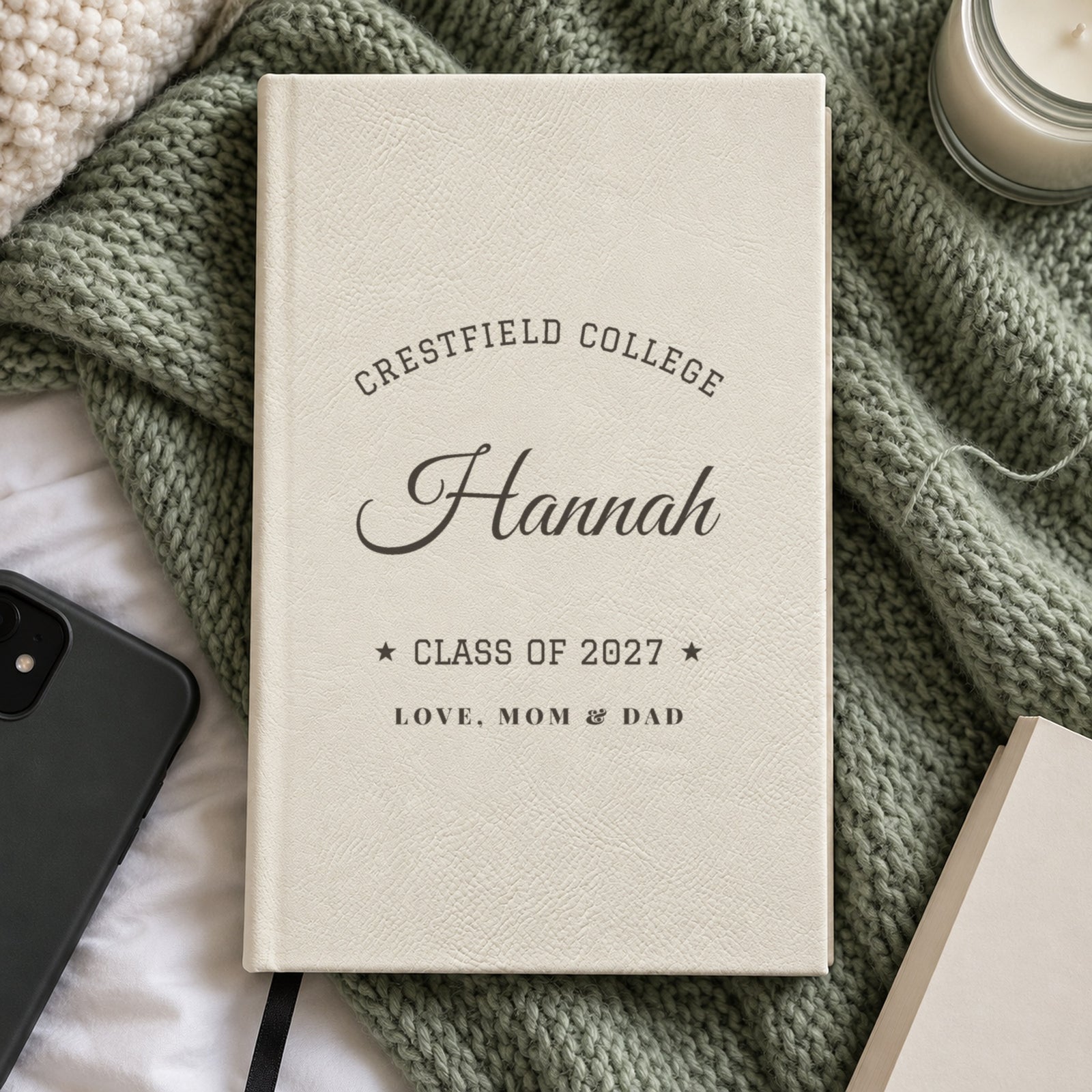 White journal engraved with Crestfield College arched over Hannah, Class of 2027 and Love, Mom & Dad, on a sage knit blanket, a gift for a daughter in college