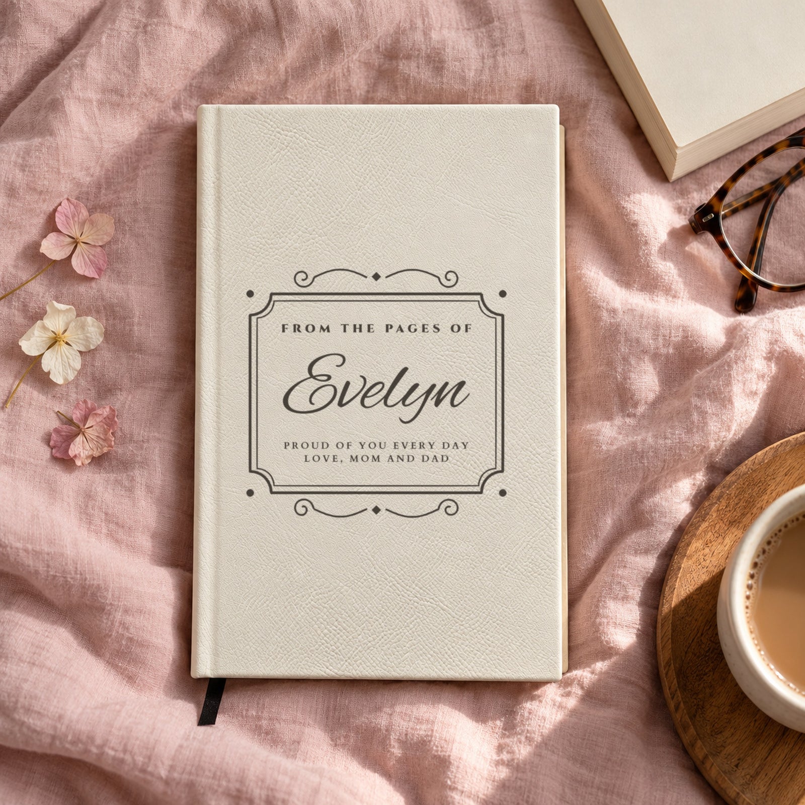 White personalized journal on a blush linen bed, engraved with Evelyn and a two line message, Proud of You Every Day, Love, Mom and Dad